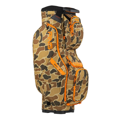 The Ping Traverse 214 Golf Cart Bag features a camouflage pattern, orange accents, multiple zippered pockets, and full-length dividers. The bag stands upright against a white background.