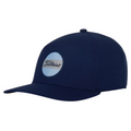 The Titleist Junior Boardwalk Cap features a navy blue design with a flat brim and a circular light blue patch with cursive Titleist branding—an ideal, stylish addition to any junior golfer’s gear.