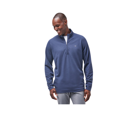 A man wears the Travis Mathew Mens Upgraded Pullover in navy and light gray pants, smiling and looking down to his left against a white background.