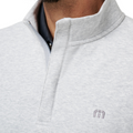 Close-up of a person wearing the Travis Mathew Cloud 1/4 Zip 2.0 Men’s Pullover in Heather Light Grey, featuring a lightweight, ultra-soft fabric, standing collar, partially open zipper revealing a dark shirt, and an embroidered chest logo.