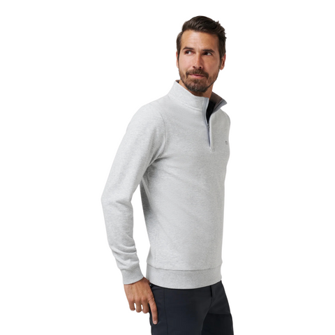 A man with short brown hair and a beard wears a Travis Mathew Cloud 1/4 Zip 2.0 Mens Pullover in Heather Light Grey and dark pants, standing against a plain white background and looking off to his left.