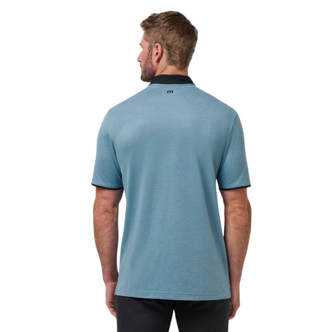 A man, seen from behind against a white background, wears the Travis Mathew Featherweight Pocket Mens Polo in light blue with a dark collar and cuffs, crafted from ultra-light performance fabric and inspired by the original TravisMathew polo.