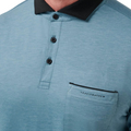 Close-up of a person wearing the Travis Mathew Featherweight Pocket Mens Polo, made from ultra-light performance fabric, with a black collar, three buttons, and a chest pocket featuring the brand name above it.