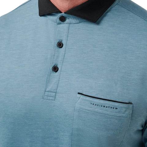 Close-up of a person wearing the Travis Mathew Featherweight Pocket Mens Polo, made from ultra-light performance fabric, with a black collar, three buttons, and a chest pocket featuring the brand name above it.