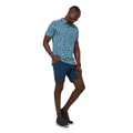 A man stands smiling with one hand in his pocket, wearing the TravisMathew Jungle Polo Shirt by Travis Mathew, dark blue shorts, black sneakers, and a wristwatch against a white background.