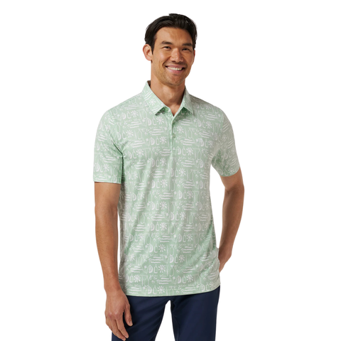 A man smiles in a TravisMathew Men’s Featherweight Cabana Polo in Aqua Foam, a stylish short-sleeve golf shirt with a modern pattern, standing with one hand in his pocket against a plain white background.