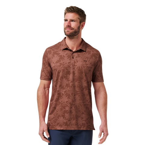 A man with short brown hair and a beard wears the Travis Mathew Mens Featherweight Ticket Polo Shirt in Maple, styled with navy pants, standing against a white background.