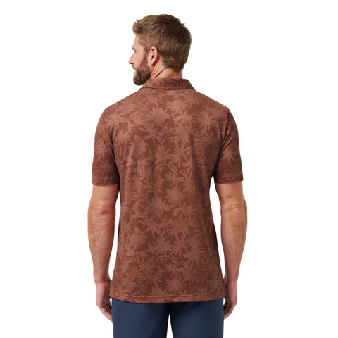 A man with short hair and a beard is seen from behind, wearing the Travis Mathew Men's Featherweight Ticket Polo Shirt in Maple and dark pants, standing against a white background.