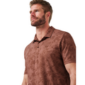 A man with light brown hair and a beard wears the TravisMathew Men's Featherweight Ticket Polo Shirt in Maple, featuring a subtle leaf pattern.