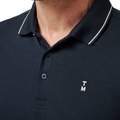 Close-up of a person wearing the Travis Mathew Mens Featherweight Ticket Polo Shirt in Total Eclipse Navy, featuring a collared neckline with white trim, two buttons undone, and small white T M initials embroidered on the left chest.