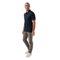A man stands against a white background wearing the TravisMathew Mens Featherweight Ticket Polo Shirt in Total Eclipse Navy, along with light brown pants and white sneakers. He faces slightly to the side in a relaxed posture.
