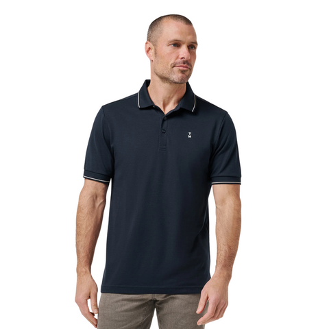 A man stands against a white background wearing gray pants and the TravisMathew Mens Featherweight Ticket Polo Shirt in Total Eclipse Navy, combining comfort and style thanks to its performance fabric.