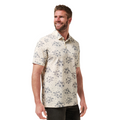 A man with short hair and a beard smiles and looks to the side against a plain white background, wearing the TravisMathew Mens Local Forecast Polo Shirt in Birch by Travis Mathew, featuring a blue floral pattern.