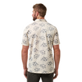 A man with short hair and a beard, seen from behind, wears a TravisMathew Mens Local Forecast Polo Shirt in Birch by Travis Mathew, featuring a blue floral pattern, paired with dark pants.