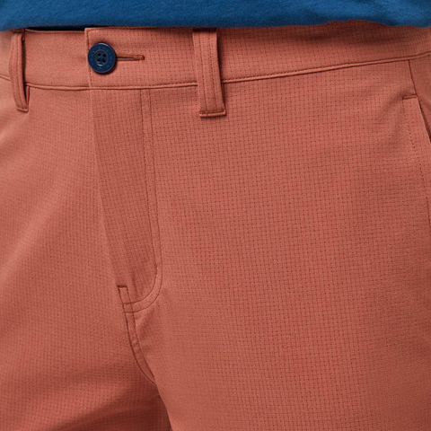 Close-up of a person wearing TravisMathew Men's Step Dance 9 Shorts in Maple, featuring a blue button and belt loops, paired with a tucked-in blue shirt.
