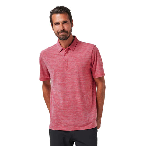 A man with short brown hair and a beard wears the TravisMathew Mens The Heater Polo in Heather Scooter, paired with dark pants, smiling as he stands against a plain white background.