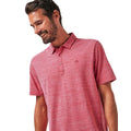A smiling man with short brown hair and a beard wears the Travis Mathew Mens The Heater Polo in Heather Scooter, a breathable performance shirt with subtle stripes, against a plain white background.