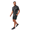A man smiles while walking, wearing the Travis Mathew Trek Tide Mens Polo—a black short-sleeve shirt with a starfish pattern—paired with black shorts and dark sneakers. The background is white.