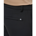 A close-up shows a person wearing the Travis Mathew Open To Close Men’s Jogger in black, featuring a welt pocket and metallic M logo, paired with a beige top for all-day comfort.