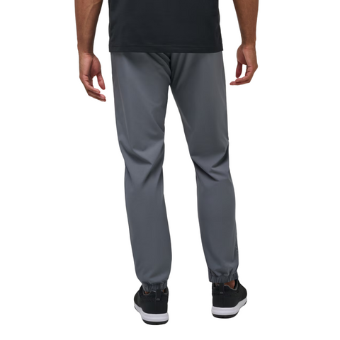 A man faces away from the camera in TravisMathew Open To Close Men's Jogger by Travis Mathew, pairing sleek gray joggers with a black shirt and sneakers.