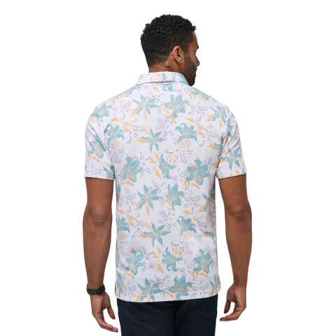 A man faces away wearing the TravisMathew Paradise Peak Men’s Polo by Travis Mathew, featuring a light blue and yellow floral pattern and dark jeans, highlighting stylish men’s golf apparel against a white backdrop.