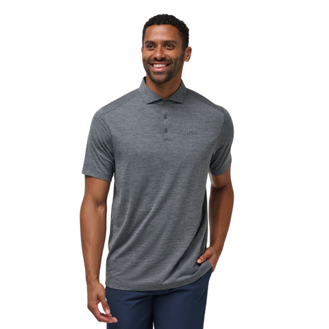 A man stands smiling against a white background, wearing the Travis Mathew The Heater Pro Mens Polo in dark gray and navy blue pants.
