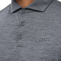 A close-up of the Travis Mathew The Heater Pro Mens Polo in gray, featuring a textured design, three buttons, a collar, and TRAVIS MATHEW embroidered on the left chest—showcasing this stylish golf polo.