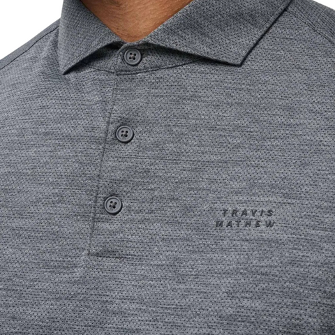 A close-up of the Travis Mathew The Heater Pro Mens Polo in gray, featuring a textured design, three buttons, a collar, and TRAVIS MATHEW embroidered on the left chest—showcasing this stylish golf polo.