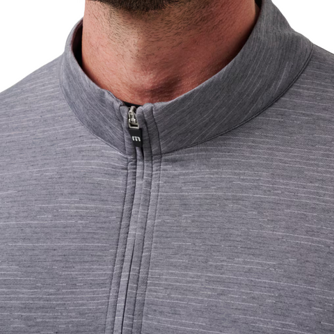 Close-up of a person wearing the Travis Mathew The Heater Quarter Zip Mens Long Sleeve Polo in gray, featuring a textured fabric and short stand-up collar. The zipper is partially closed, revealing the lower face and neck.