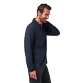 A man with short dark hair and a beard, wearing the Travis Mathew The Heater Quarter Zip Mens Long Sleeve Polo in navy and black pants, smiles and touches his neck while standing against a plain white background.