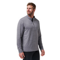 A man with short brown hair and a beard is wearing the TravisMathew The Heater Quarter Zip Mens Long Sleeve Polo in light gray and black pants, standing and looking slightly to his left against a white background.