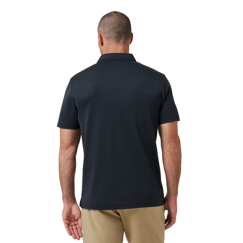 A man faces away from the camera, dressed in beige pants and the TravisMathew The Zinna 2.0 Men’s Polo in black, showcasing a casual yet polished style ideal for any setting.