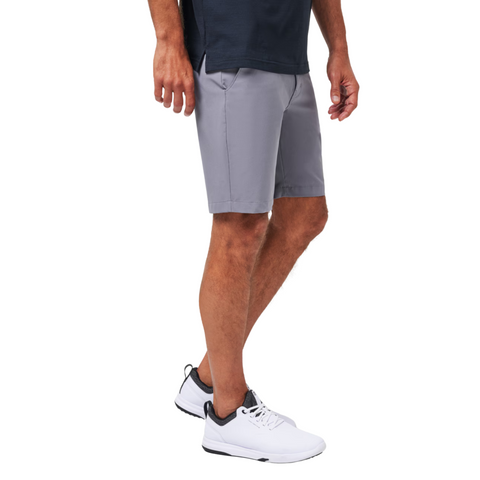 A man’s lower body is shown wearing Travis Mathew Wanderlust Mens Shorts, paired with a navy shirt and white sneakers with black accents, set against a plain white background to highlight the stylish golf shorts.