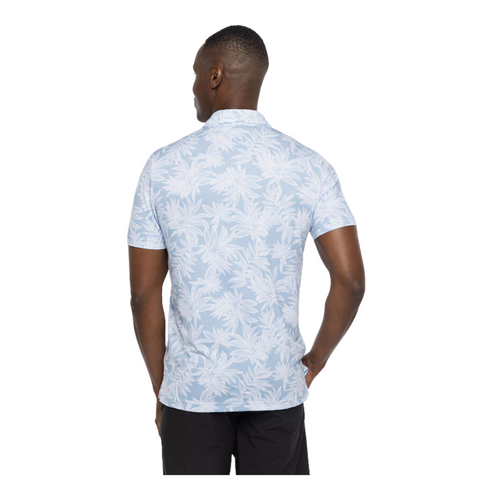 Side view of a model wearing the TravisMathew Sea Journey Polo, light blue with a white tropical leaf print, short sleeves, and a relaxed fit for casual, comfortable wear.