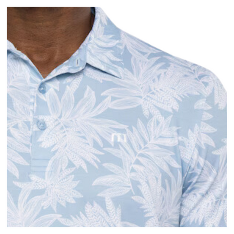 Close-up view of the TravisMathew Sea Journey Polo, showcasing the light blue fabric with a white tropical leaf pattern. The shirt features a three-button placket and a soft collar, highlighting the intricate detailing of the design.