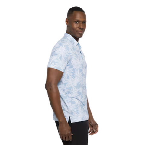 Side view of a model wearing the TravisMathew Sea Journey Polo. The light blue polo features a tropical leaf print, short sleeves, and a relaxed fit, offering a casual yet stylish look ideal for warm weather.