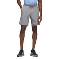 The Adidas Ultimate365 8.5-Inch Men's Golf Shorts in grey, worn by a model, front view. Features a tailored fit with side pockets and a belt, paired with black Adidas golf shoes