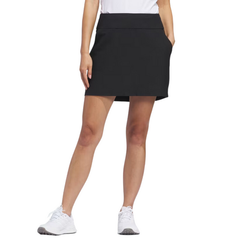 Front view of the black Adidas Ultimate365 Solid Women's Skort, shown with white athletic shoes. The skort has a fitted waistband and falls above the knee.