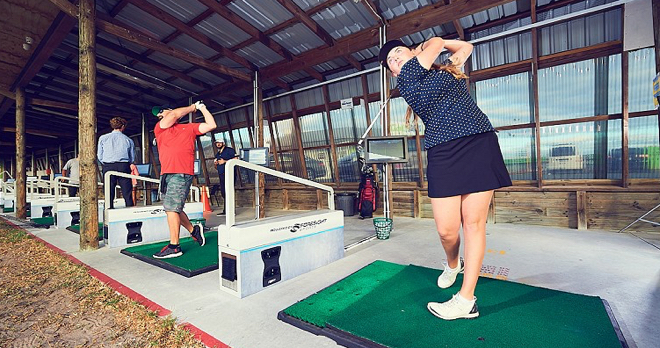 Two golfers swing their clubs back after hitting balls in a driving range.