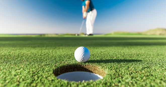 A golf ball rests at the edge of a hole on a golf green.