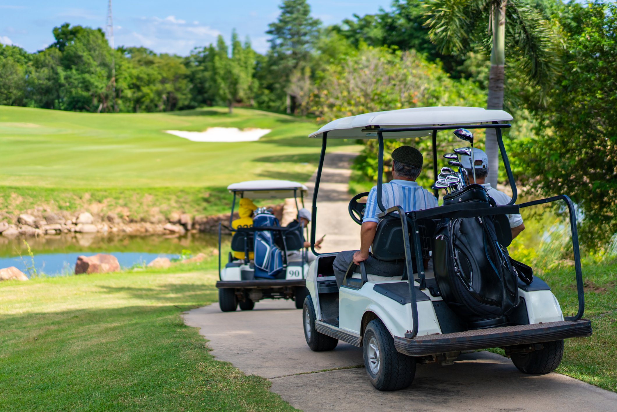 Two golf carts with people in them driving along a golf course.