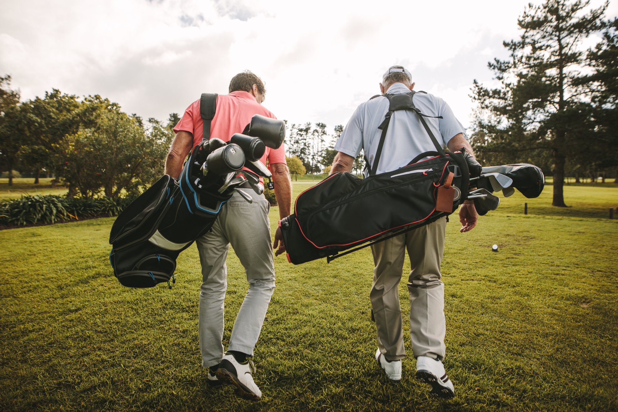 Two men with golf bags walking on a golf course.