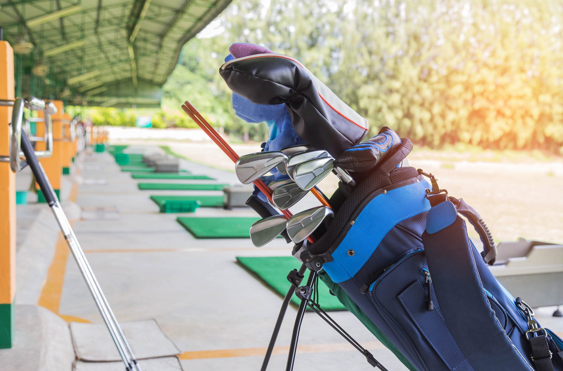 A golf cart filled with golf clubs standing at a driving range.