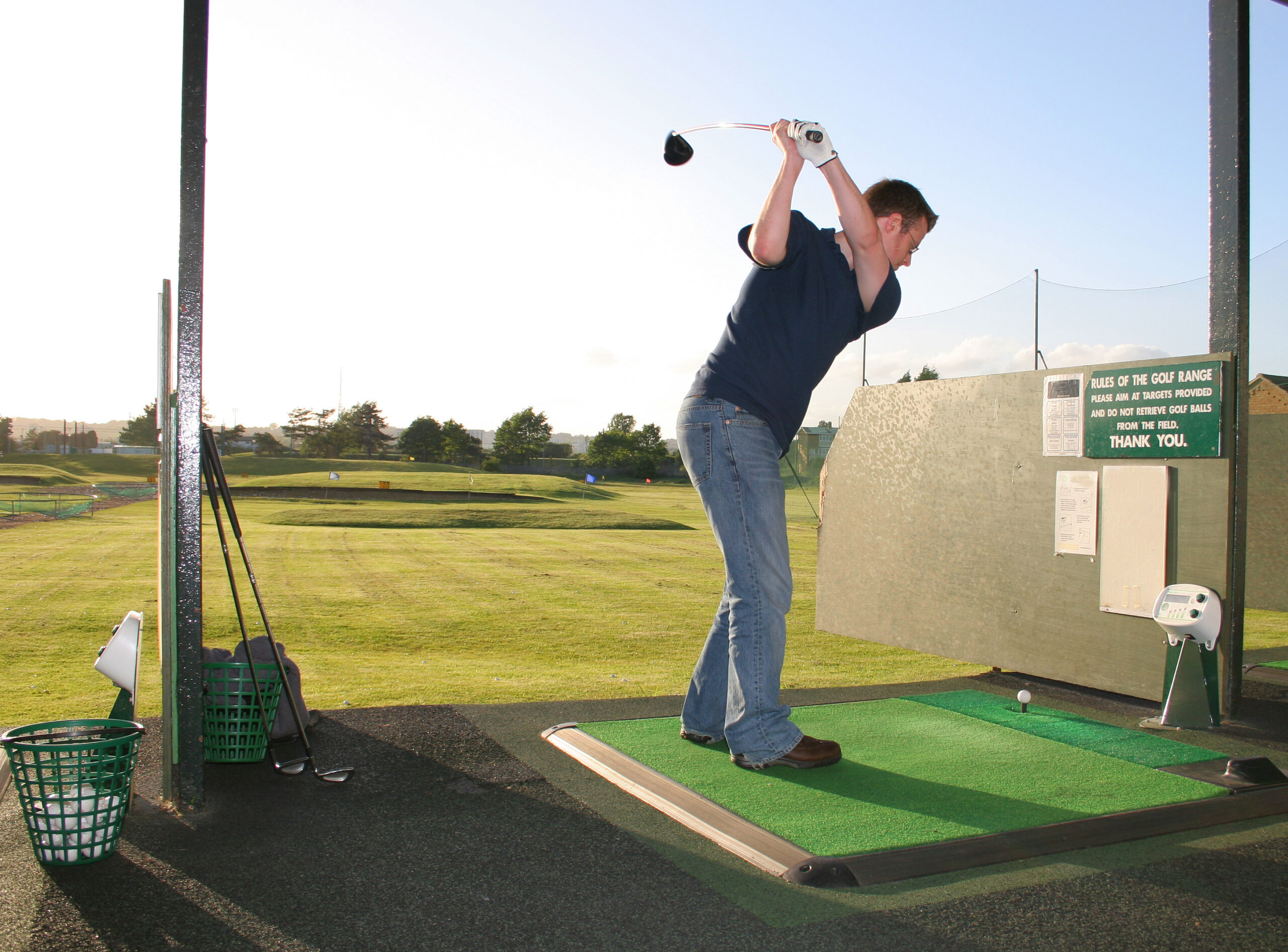An image of a man hitting golf balls at a driving range.