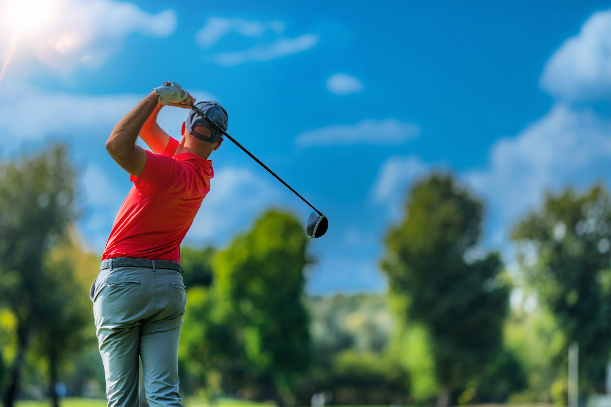 A man wearing a red shirt is playing golf.