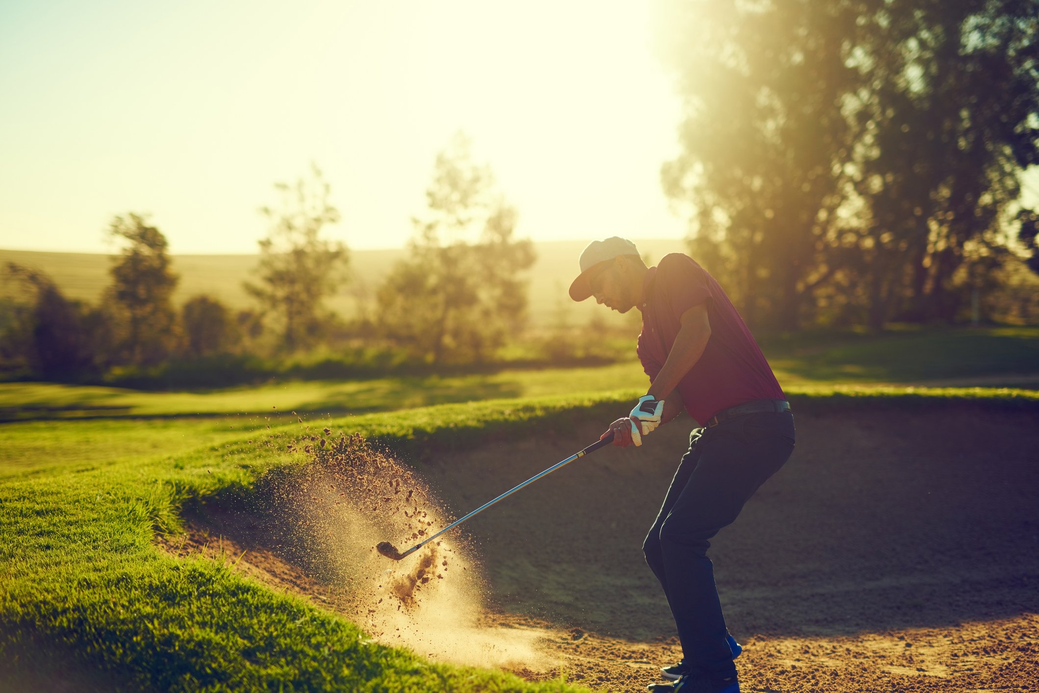 Shot of a young man hitting the ball out of the bunker during a round of golf.