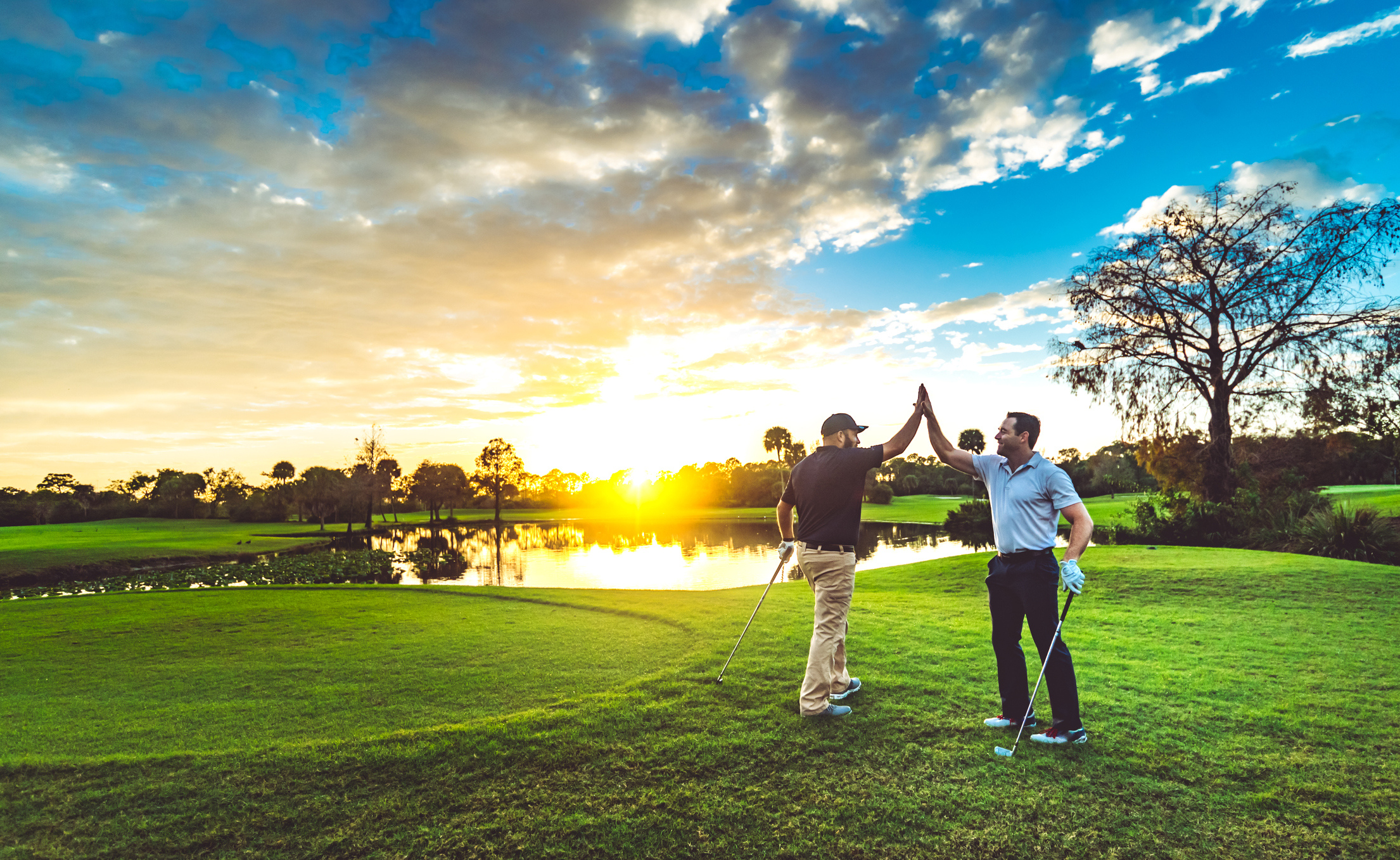 Two male golfers high five on a scenic sunset golf course.